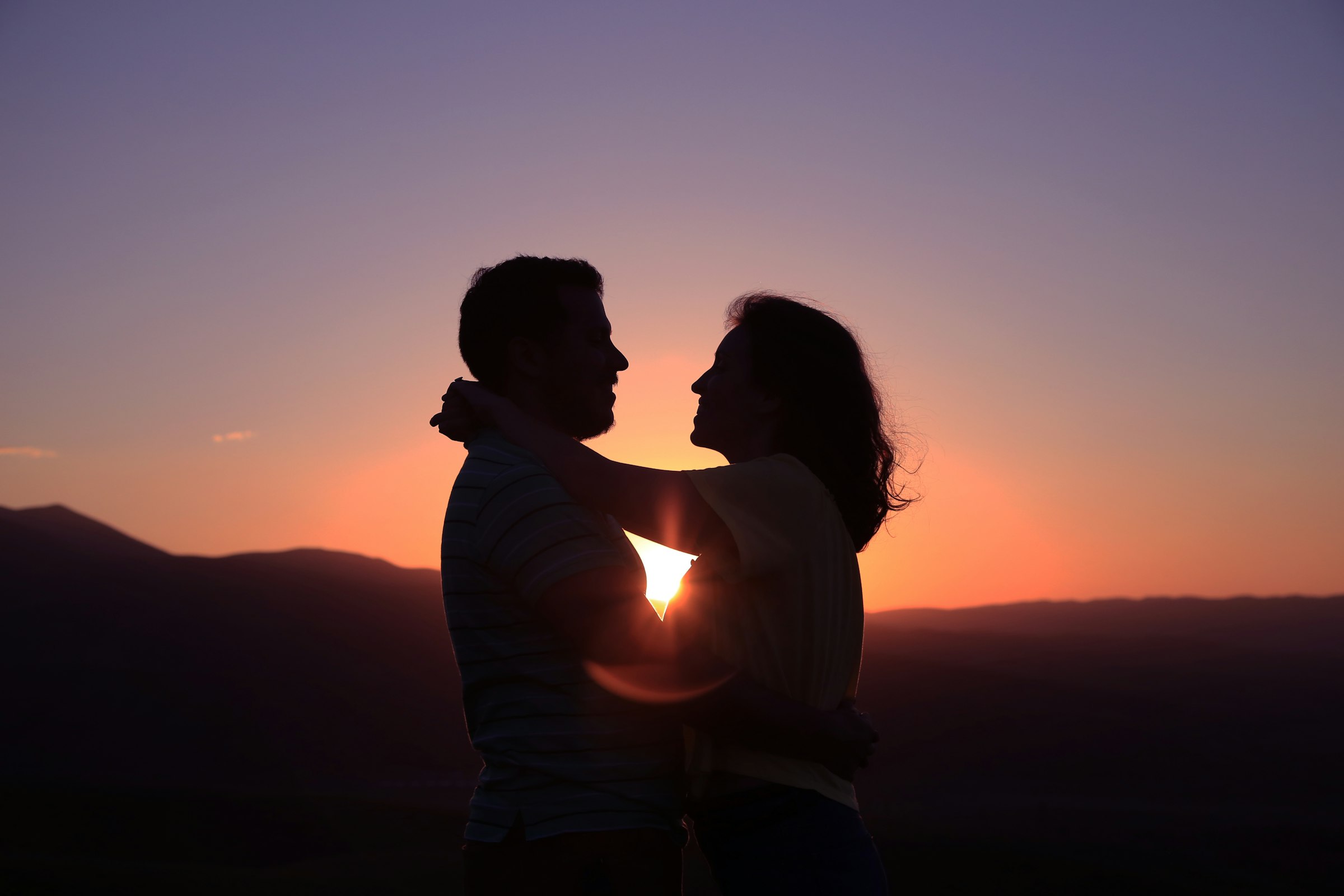 Silhouetted couple embracing against a colorful sunset over distant hills