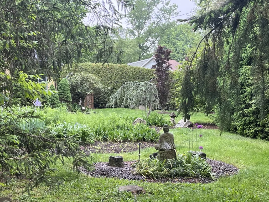 Lush garden with trees, flowering plants, and a small statue