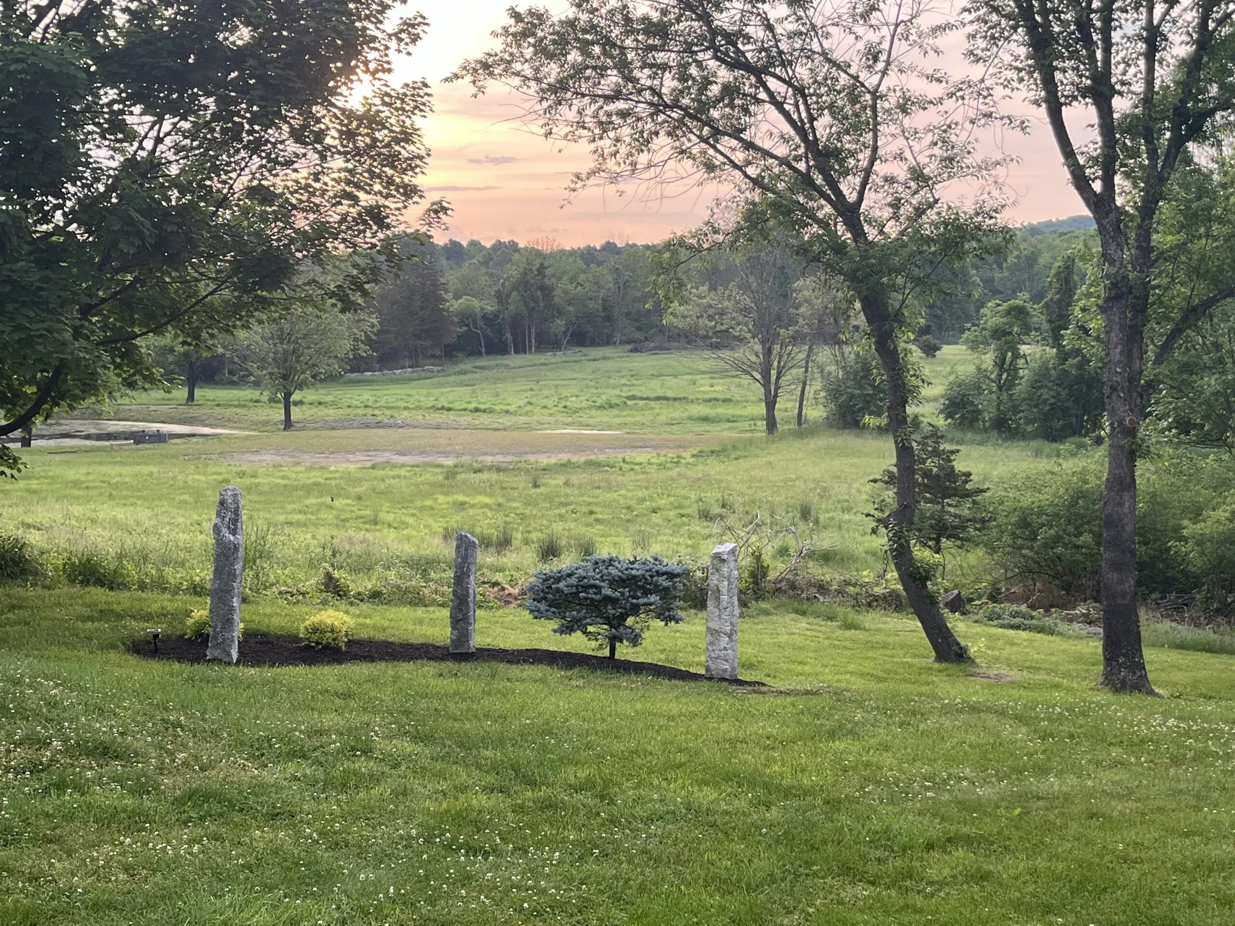 Three stones in a garden overlooking a field at sunset