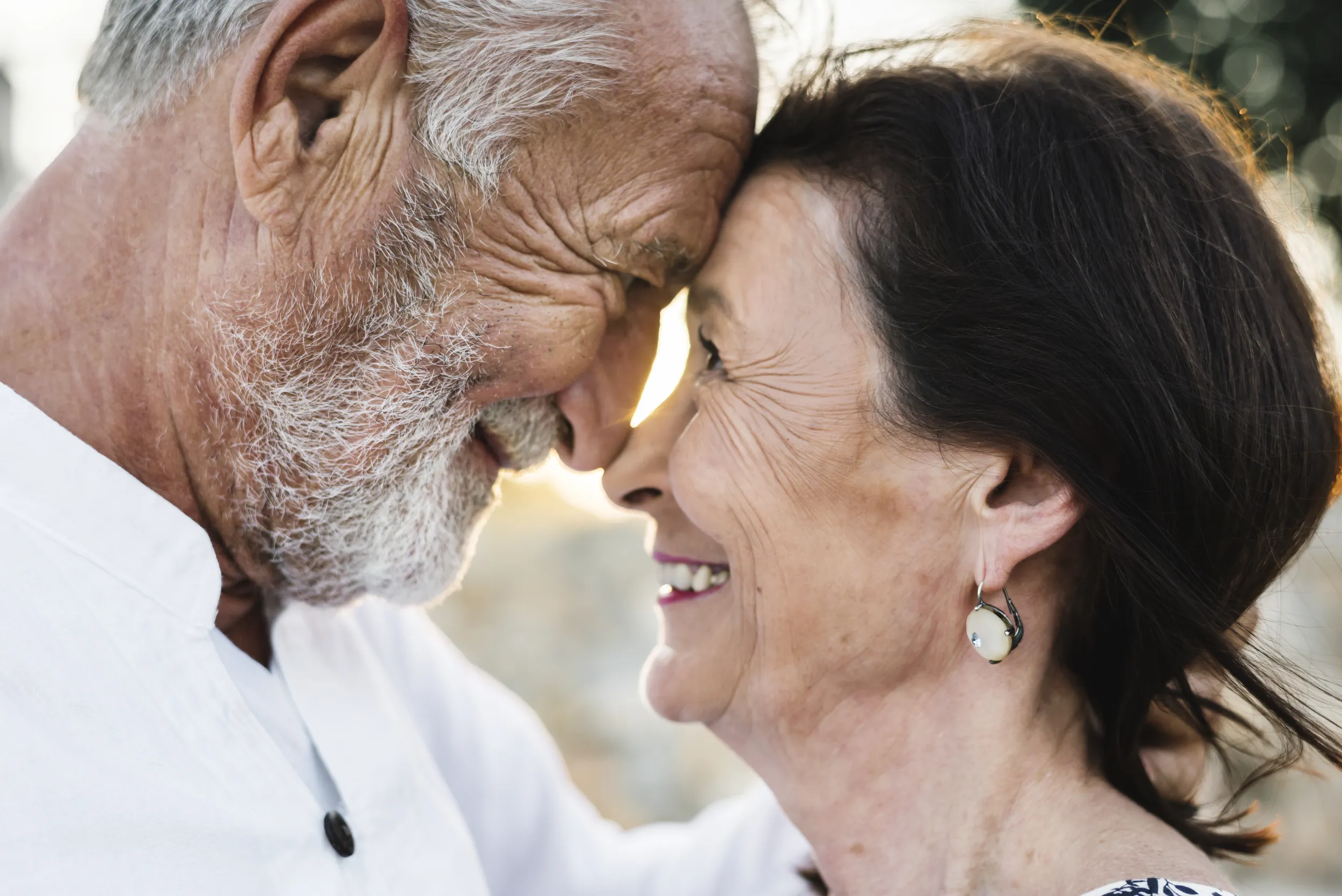 Older couple smiling with their foreheads touching in warm golden light